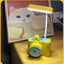 Yellow camera-shaped night light on a wooden surface with a cat illustration in the background.