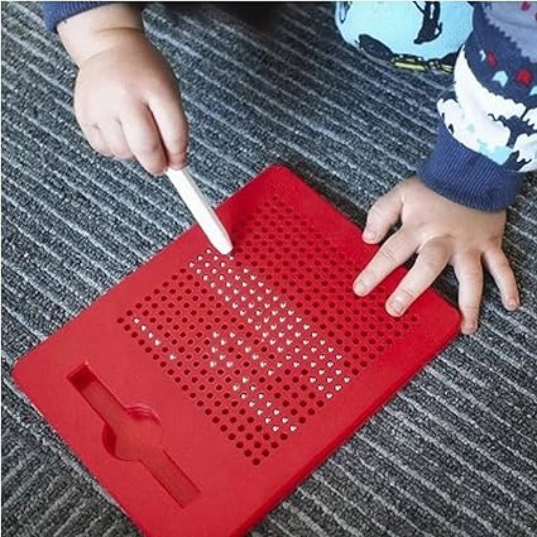 Red silicone mat with holes on a textured surface, child's hands interacting with it.