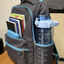 Gray backpack with blue accents on a wooden surface, containing books and a water bottle.