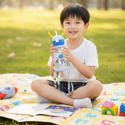 Child sitting on a colorful blanket in a park holding a water bottle.
