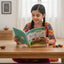 Young girl reading a book at a table with colorful toys around
