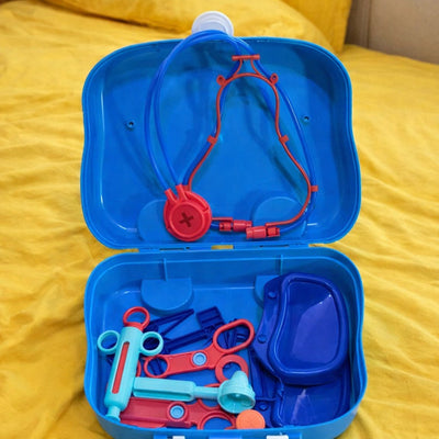Toy medical kit with stethoscope and other tools in a blue case on a yellow blanket.