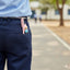 Person wearing navy pants with a pink pen and keychain in the pocket, blurred outdoor background