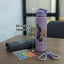 Pink water bottle with challenge design, gray towel, small pouch with bands, and carabiner on a table.