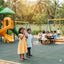 Children playing on a playground with slides and swings in a park setting.