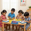 Four children sitting at a table in a classroom setting, engaged in an activity with colorful materials.