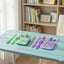 Desk with stationery items including pens, a ruler, and a purple case in a room with a bookshelf.