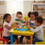 Four children playing with toys at a colorful table in a classroom setting.