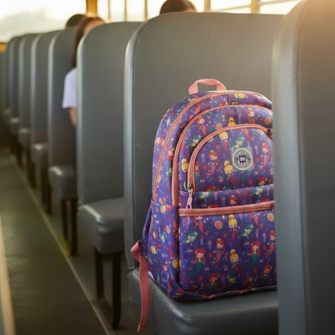 Colorful backpack on a school bus seat with sunlight streaming through the windows.